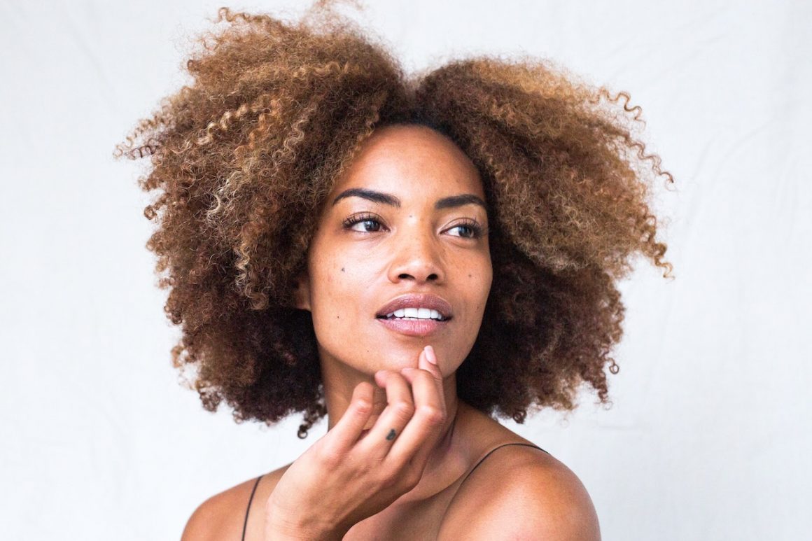 Woman with beautiful afro and soft skin strokes her face.